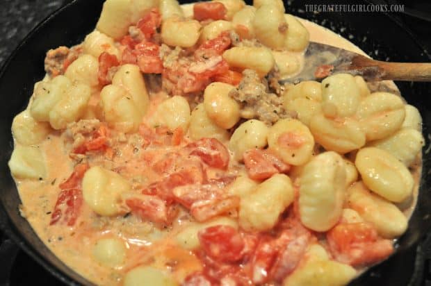 Tomatoes and cream added to gnocchi in skillet