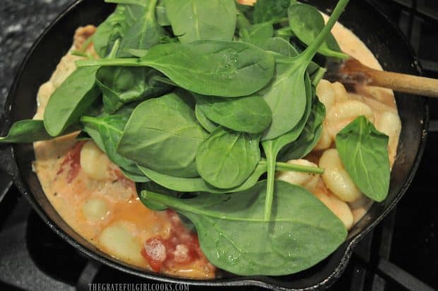 Fresh spinach added to cast iron skillet and creamy sauce