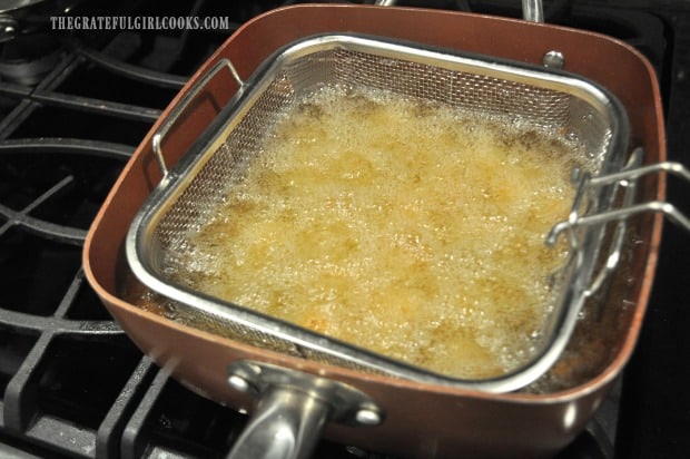 Tater tots deep frying in oil in large saucepan with fry basket