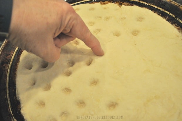 Holes poked into top of focaccia bread dough with finger