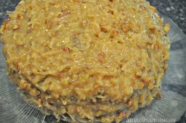 Homemade coconut pecan frosting is spread onto and covers cake