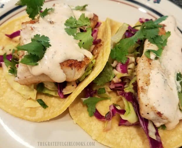 Two grilled fish tacos, with slaw and Baja sauce, on plate.