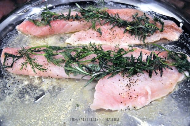 Pan-searing fish with fresh herbs in skillet