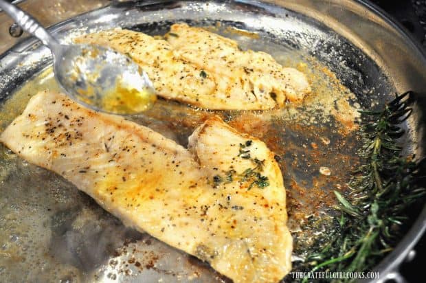 Spooning melted butter over golden brown rockfish fillets in skillet