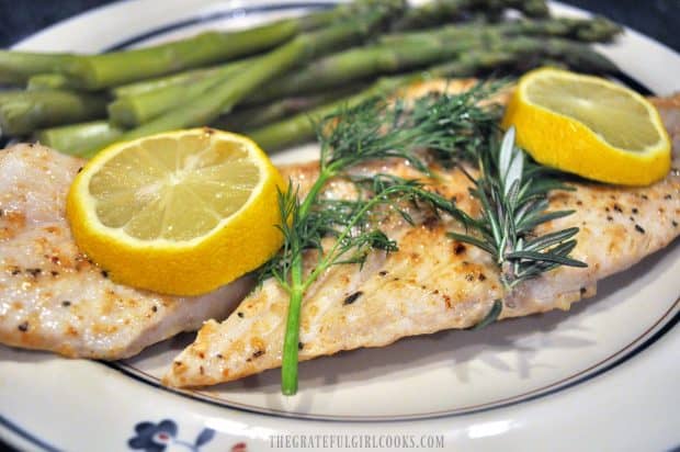 Pan-seared fish with dill, rosemary and lemon slices, on plate with asparagus.