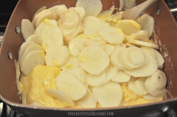 Potato slices are added to au gratin cheese sauce in pan