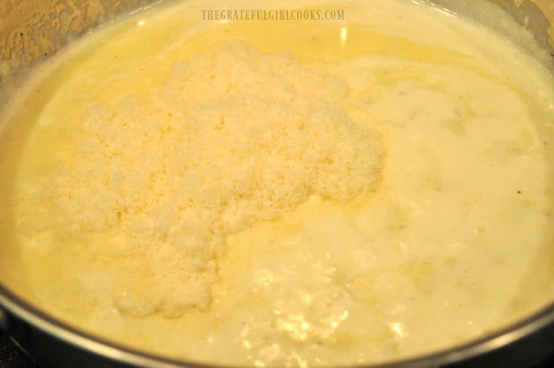 Grated Parmesan cheese is added to alfredo sauce in pan