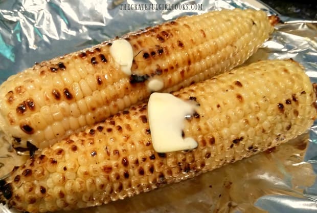 Grilled corn on the cob is done and slathered with butter