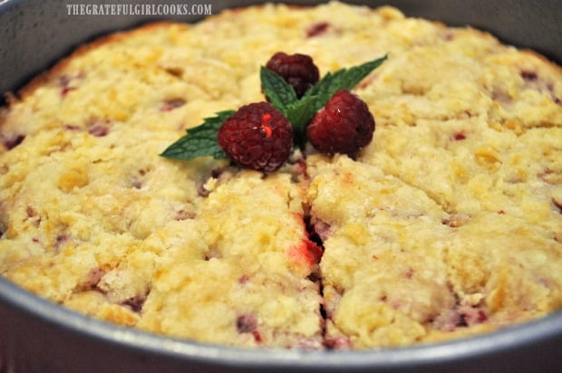 Raspberry lemon crumb cake cut in 8 wedges, garnished with raspberries and mint leaf.