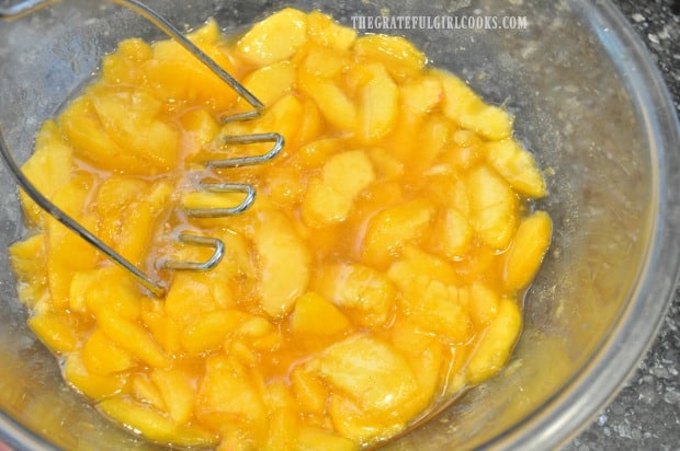 Fresh peach slices are crushed with a potato masher for ice cream