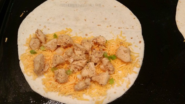 Cheese, chicken and green onions are placed on a flour tortilla half for chicken black bean quesadilla.