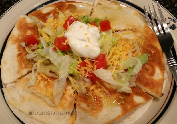 Chicken black bean quesadilla is garnished with lettuce, tomato, sour cream and salsa verde.