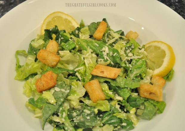 Croutons and lemon slices are added to caesar salad.