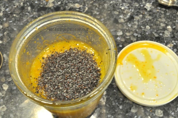 Poppyseeds are added to citrus dijon salad dressing in jar.