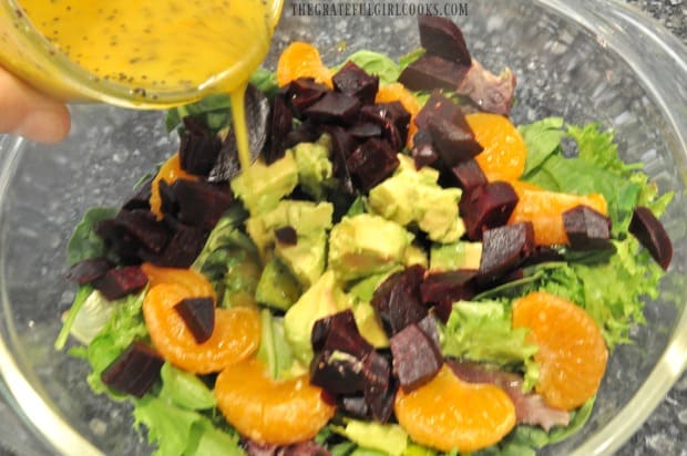 Citrus Dijon salad dressing being poured over mixed green salad.