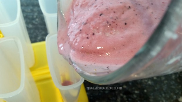 Fruit smoothie is poured into popsicle molds.