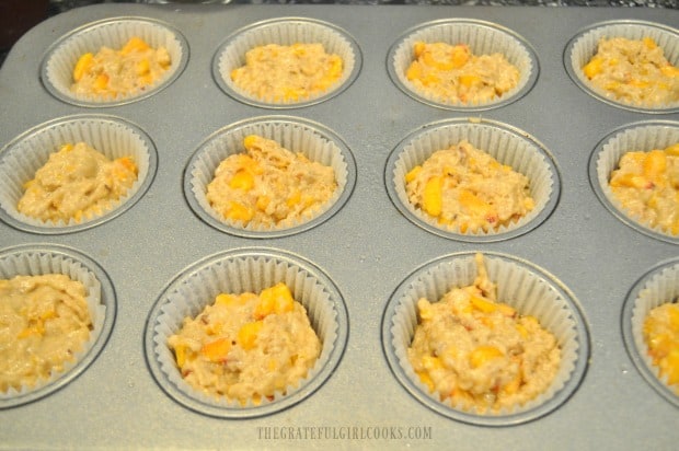 Batter for peach jam muffins is added to muffin tin for baking.