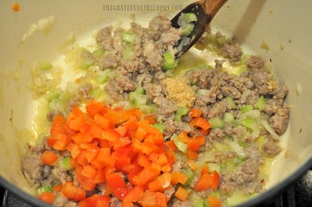 Red bell pepper and garlic added to ragu sauce in pot.