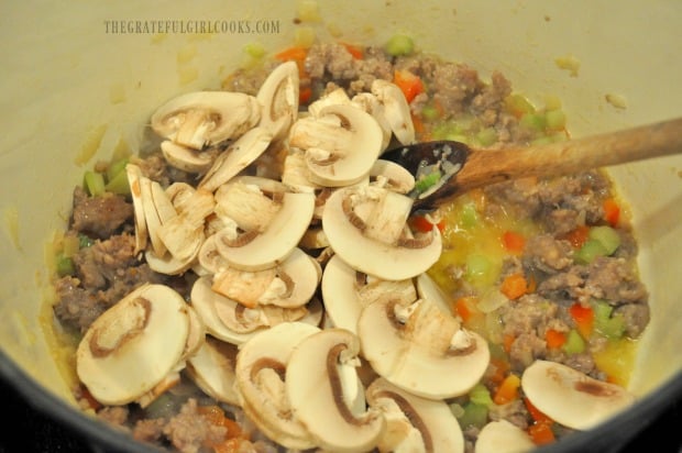 Sliced mushrooms are added to ragu sauce in pot.