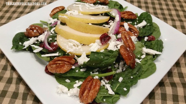 Spinach pear salad with candied pecans, on white plate.