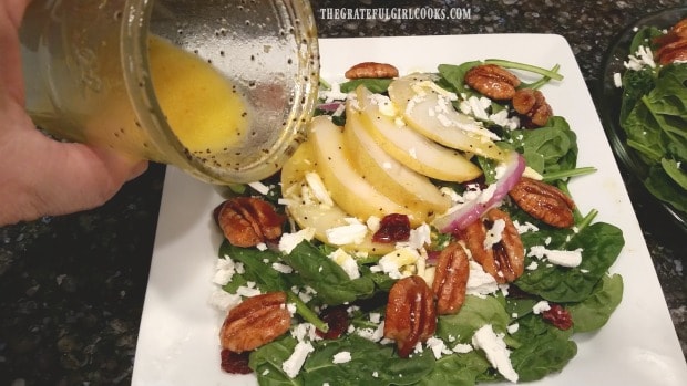 Citrus dressing is added to spinach pear salad before serving.