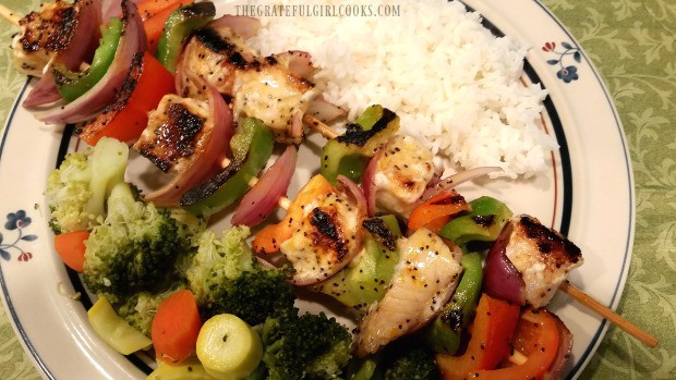 Two citrus marinated swordfish kabobs on plate with vegetables and rice on side.