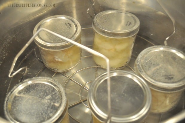 Jars of pears with lids are placed onto elevated rack in simmering water in canner.