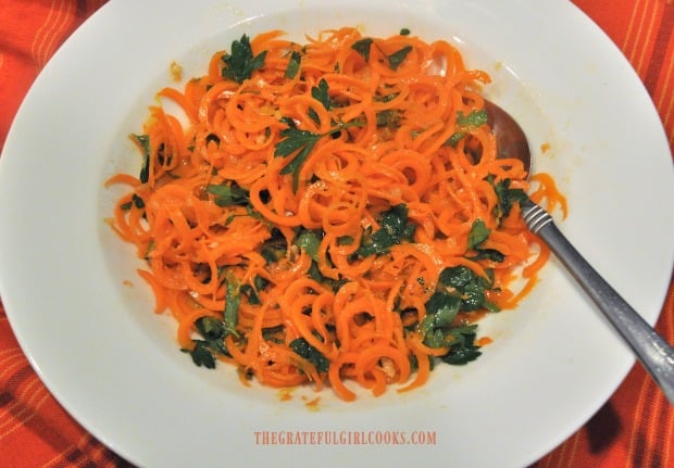 Spiralized carrot salad with lemon ginger dressing is served in a white bowl.