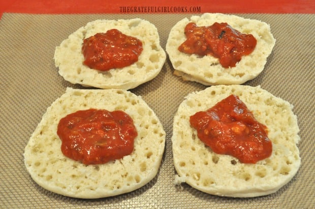 Pizza sauce is spread onto split, untoasted English muffins for mummy pizzas.