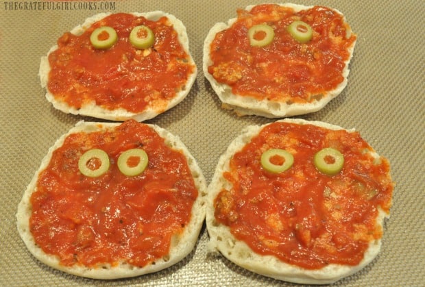 Green olive eyes are added to English muffin mummy pizzas.