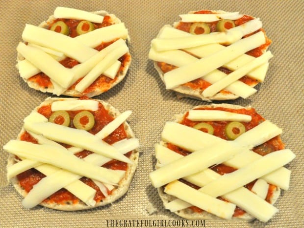 Strips of mozzarella cheese are added to English muffin mummy pizzas.