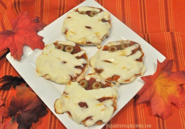 English muffin mummy pizzas on white plate, after baking in oven.