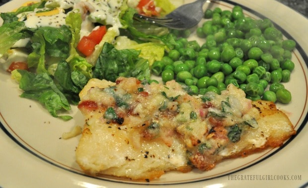 Roast cod with garlic bacon butter on a plate with peas and a green salad.