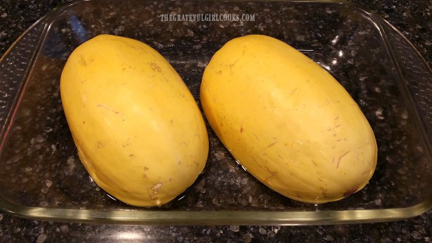 De-seeded spaghetti squash halves are placed cut side down in baking pan with water.