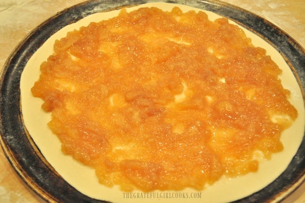 Pizza dough is topped with apple pie filling before baking, for apple pie dessert pizza.