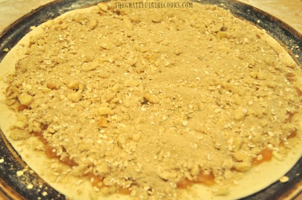 Streusel topping is placed on top of the apple pie dessert pizza, before baking.