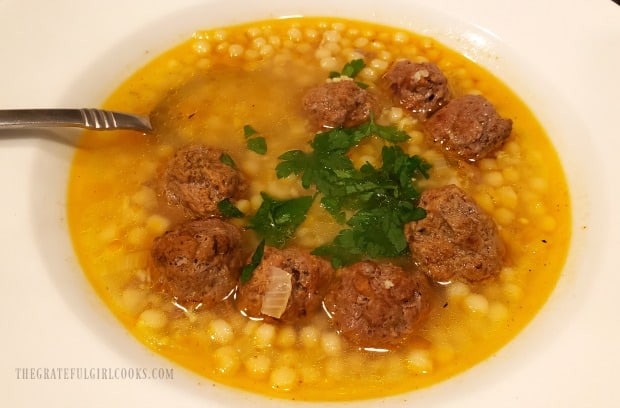 Moroccan meatball couscous soup, served in white bowl, with fresh parsley garnish.