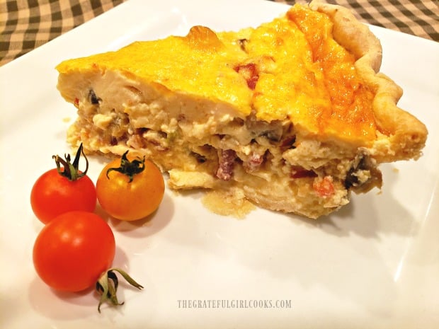 A slice of Southwestern bacon quiche, on a white plate, with a few cherry tomatoes.