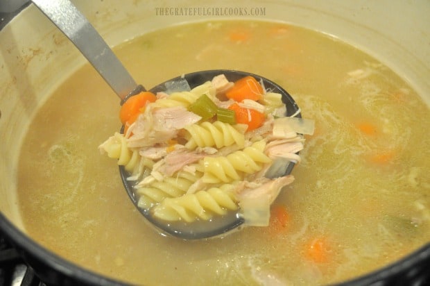 Chicken noodle soup in a ladle is almost done cooking.