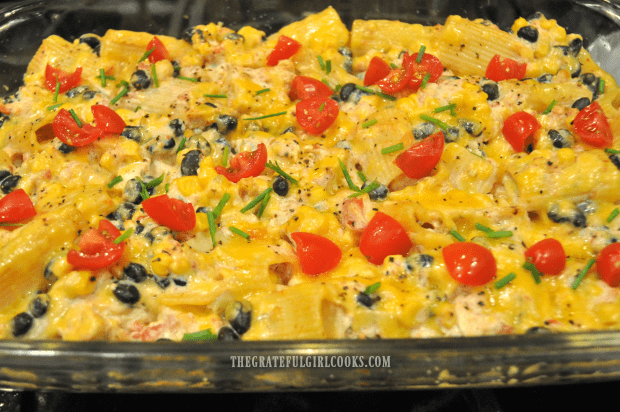 The baked fiesta chicken pasta casserole is garnished with tomatoes and chives before serving.