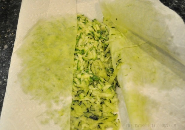 Draining shredded zucchini between layers of paper towels, to absorb moisture.