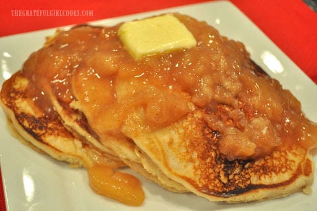 Butter and warm apple pie filling top a stack of apple pie pancakes.