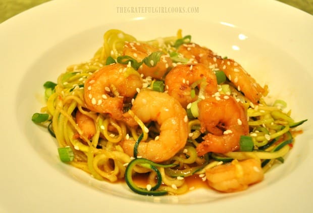 Sweet chili sesame shrimp zoodles, served with green onion garnish, in white bowl.