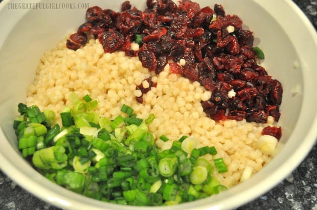 Dried cranberries and sliced green onions are added to the Israeli couscous in bowl.