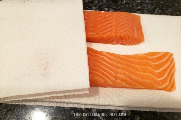 Salmon fillets are blotted dry with paper towels before cooking.