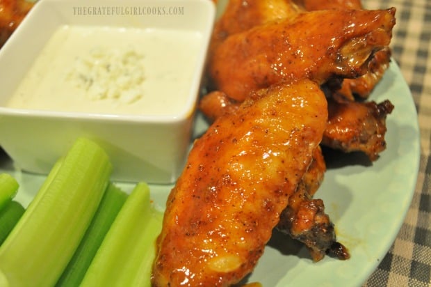 Buffalo honey hot wings on plate with celery sticks and bleu cheese dressing on the side.