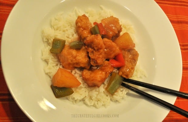 The finished sweet and sour pork is served in a bowl, on rice, with chopsticks on the side.