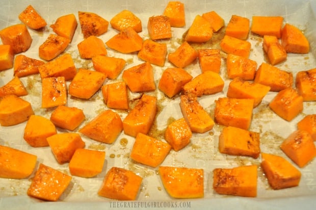 The pieces of maple cinnamon butternut squash are placed on parchment paper to bake.