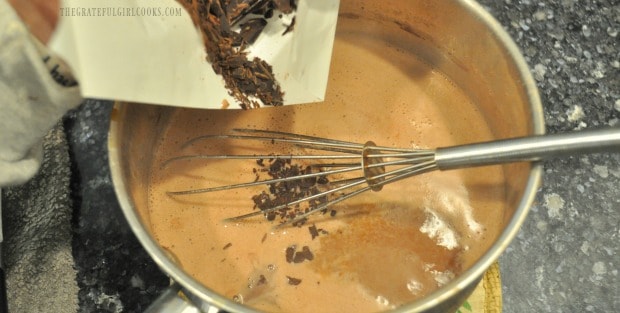 Grated bittersweet chocolate is added to hot homemade chocolate pudding mixture in pan.