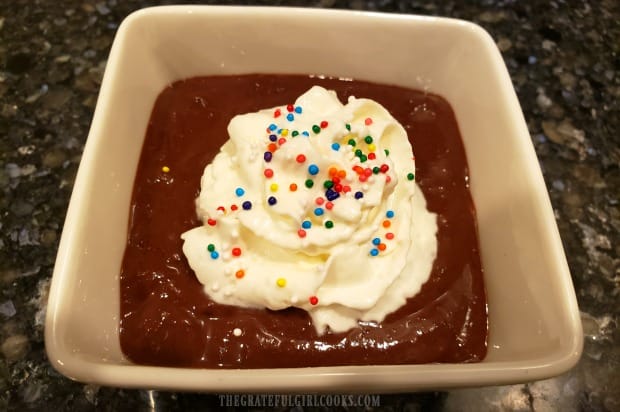The cold homemade chocolate pudding is portioned into dishes, topped with whipped cream and served.